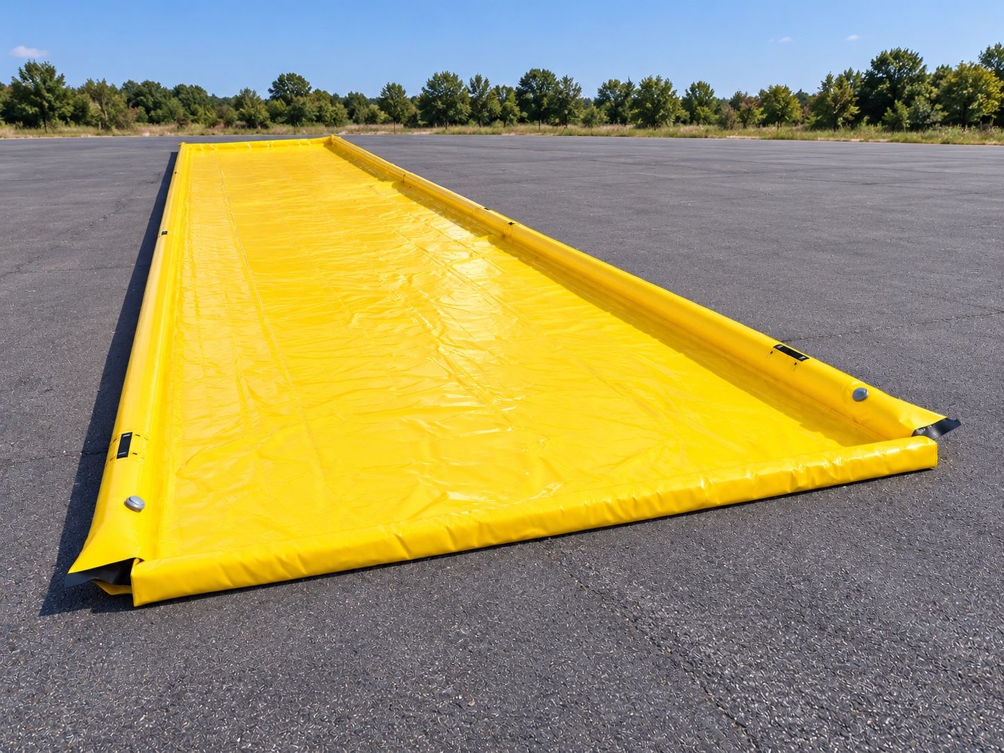 Long yellow PVC vehicle disinfection berm on tarmac, with inflated tube rims along both long sides, low open ends for vehicles to drive through, and inflation valves at the corners