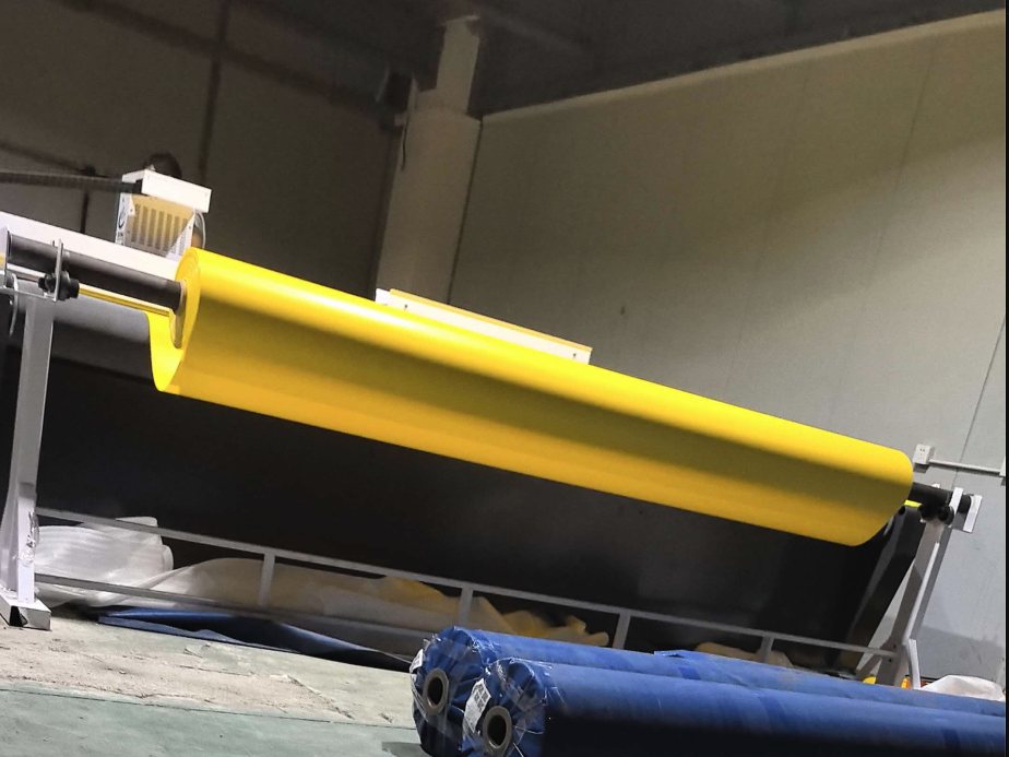 Yellow PVC-coated polyester roll on the CNC cutter, with blue fabric rolls on the floor